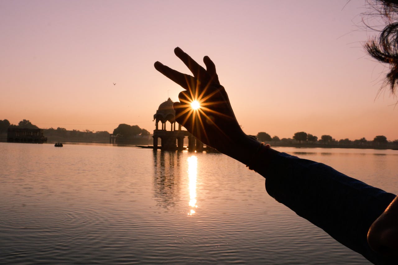 Hand silhouette with sunrays over Indian lake at sunset, creating a peaceful and artistic view.