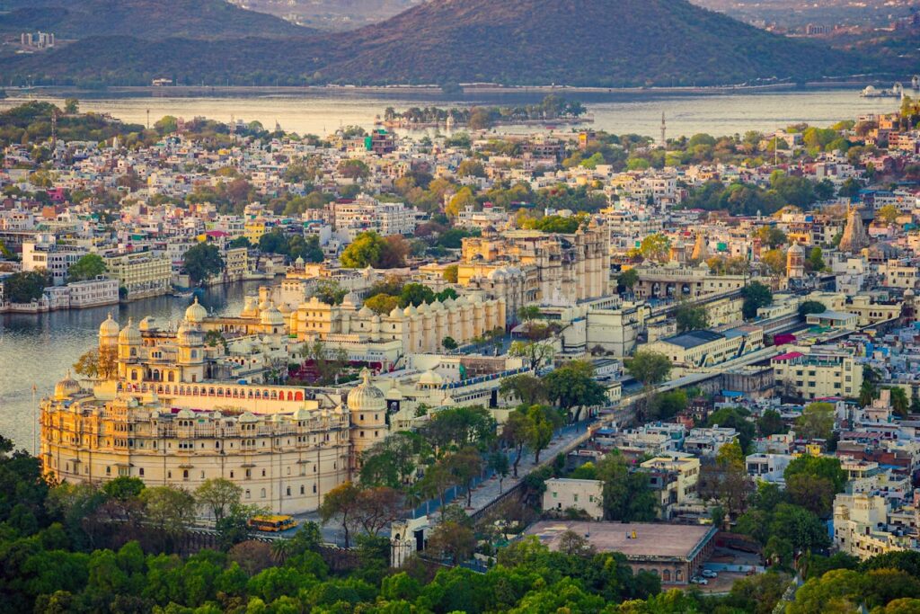 pexels-photo-18526644 Aerial view of the historic Udaipur City Palace and surrounding cityscape against a tranquil lake backdrop.